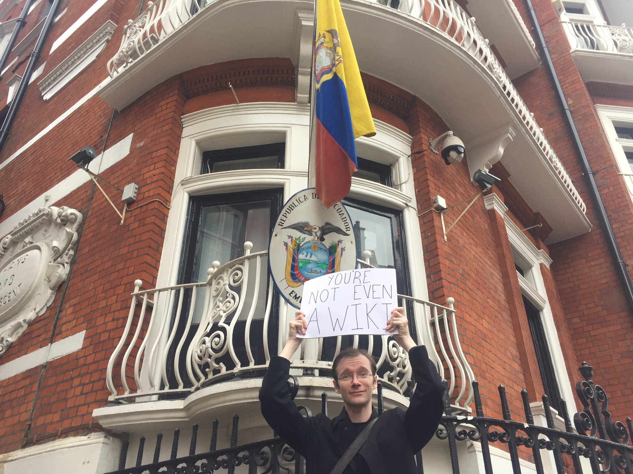 Garrett in 2016, standing outside the Ecuadorian Embassy in London holding a sign saying